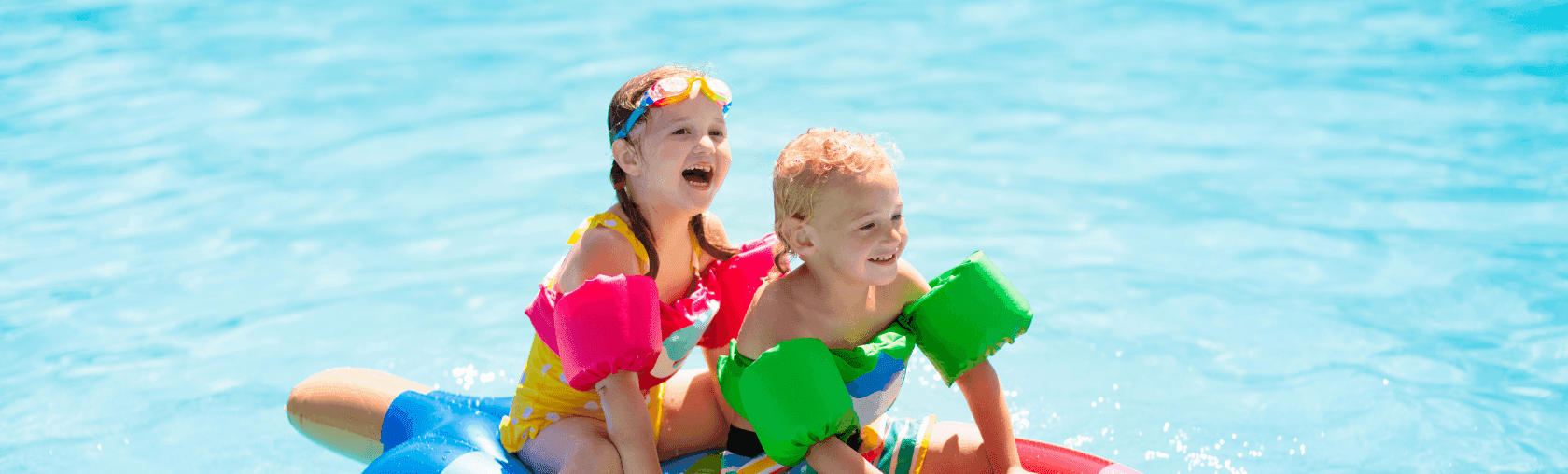 Two happy children, a girl and boy, play on an inflatable in a blue swimming pool.
